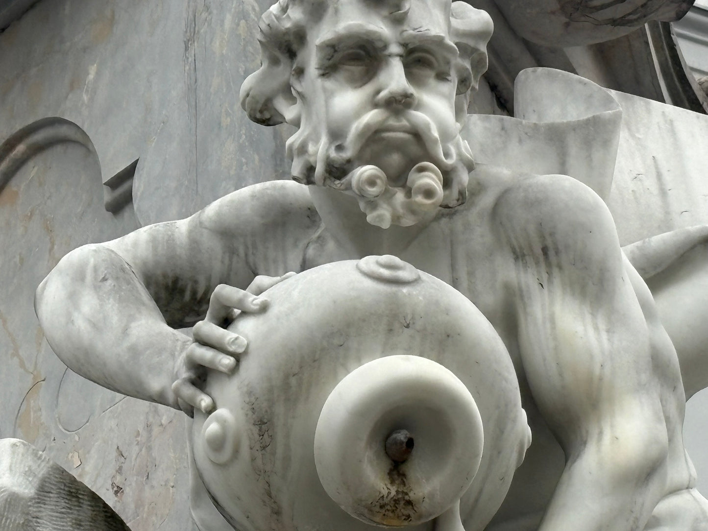 Eine Nahaufnahme einer barocken Marmorskulptur, die Teil des Robba-Brunnens (auch Brunnen der drei kranjischen Flüsse genannt) in Ljubljana, Slowenien, ist.
Zentrales Motiv: Die Skulptur zeigt einen kräftigen, muskulösen Mann mit einem vollen, lockigen Bart und intensivem Gesichtsausdruck. Er blickt leicht nach rechts oben.
Aktion: Die Figur hält mit beiden Händen einen großen, bauchigen Krug (Amphore) vor ihren Körper. Die linke Hand liegt oben auf dem Krug, während die rechte Hand ihn seitlich stützt.