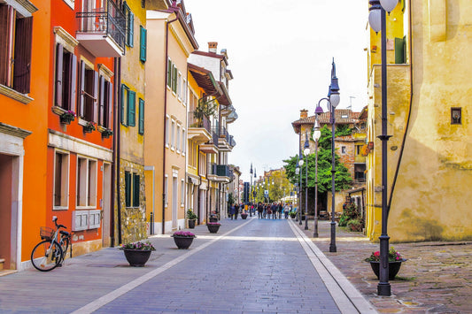 autofreie Promenade mit bunten Häusern links und rechts. auf der linken Seite steht ein Fahrad, auf der rechten Seite in regelmäßigen Abständen Straßenlaternen. Am Ende der Promenade spaziert eine Gruppe junger Menschen.