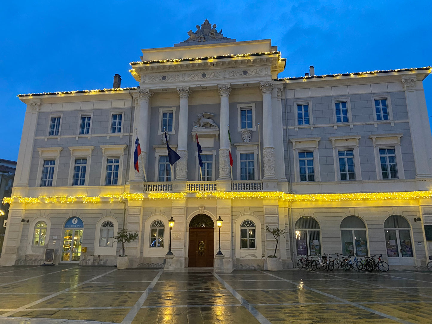Rathaus von Piran hell beleuchtet in der Abendstimmung mit mehreren Fahnen wie slowenische und italienische Fahne sowie die Fahne der EU