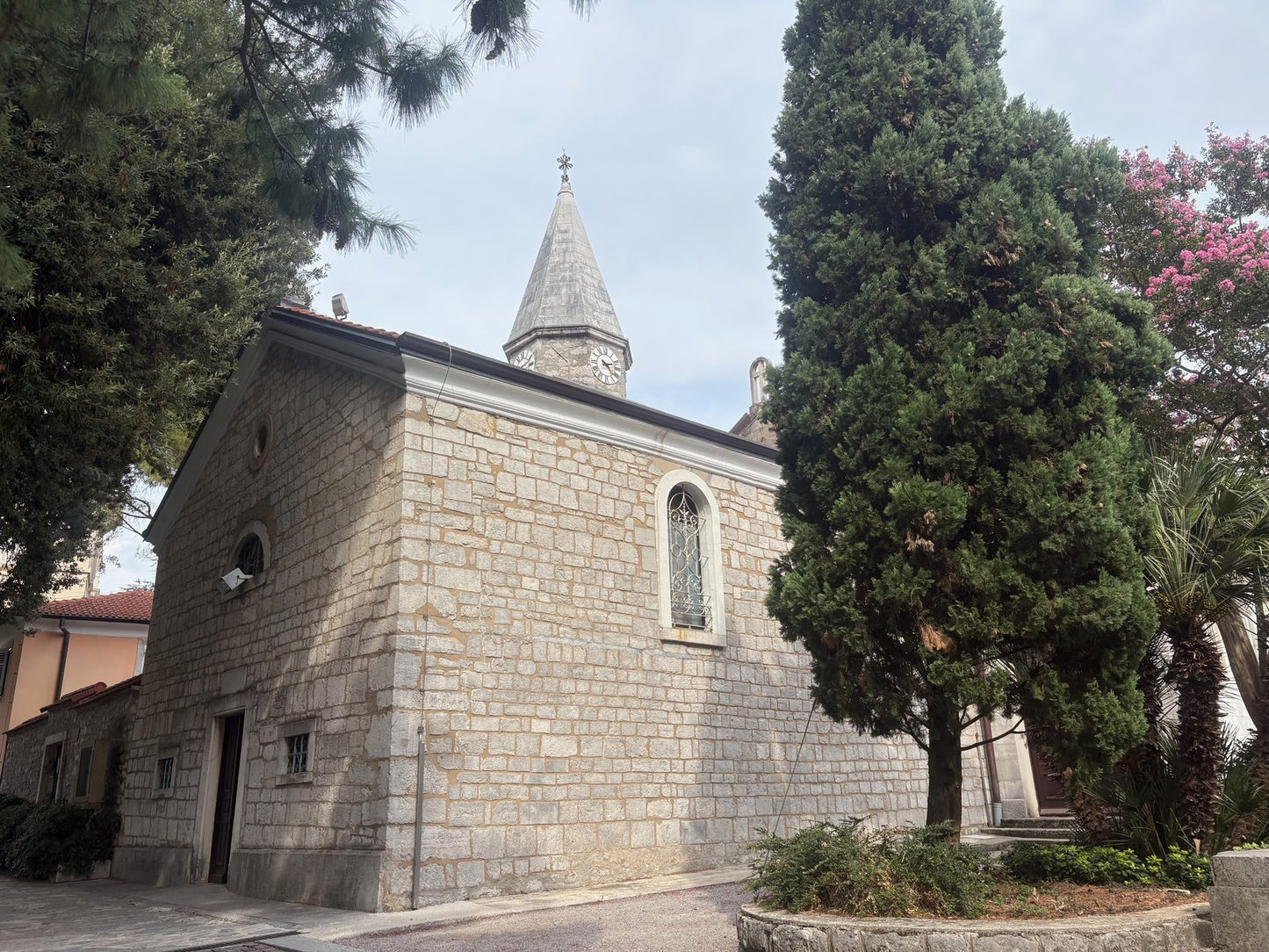 Die Abteikirche Crkva sv. Jakova in Opatija aus hellem Stein, daneben hohe Zypressen und blühender Oleander.