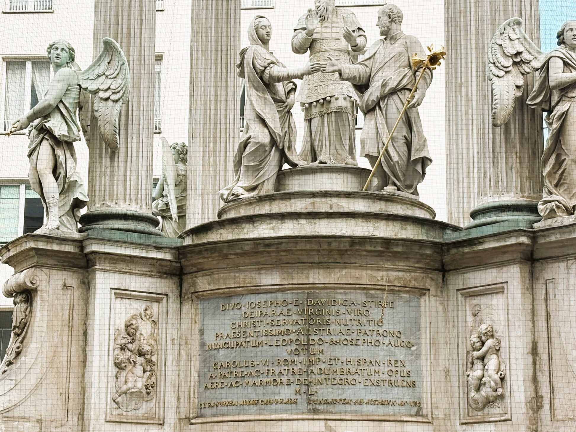 Eine Nahaufnahme einer der Skulpturen am Vermählungsbrunnen auf dem Hohen Markt in Wien.

Zu sehen ist ein muskulöser, bärtiger Mann in barockem Stil, der einen großen Krug (eine Amphore) hält, aus dem Wasser fließt.

Die Skulptur ist detailreich aus hellem Stein gearbeitet, wobei die dynamische Pose und die Gesichtszüge des Mannes im Fokus stehen.

Im Hintergrund ist die klassizistische Architektur des Brunnenaufbaus zu erkennen.