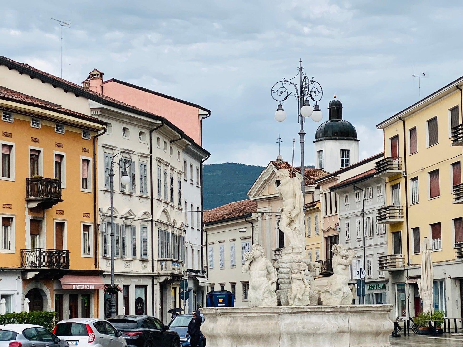 Neptunbrunnen an der Piazza della Vittoria in Görz mit Häusern links und rechts davon.