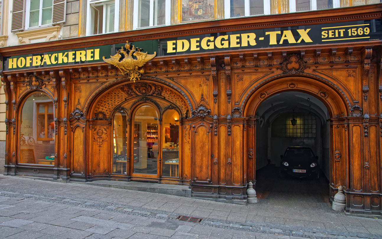Historische Holzfassade der Hofbäckerei Edegger-Tax in der Grazer Sporgasse mit dem goldenen Doppeladler der k.u.k. Monarchie. Traditionelles Grazer Handwerk und Architektur-Sehenswürdigkeit in der Steiermark – ixpirity: feel the city.