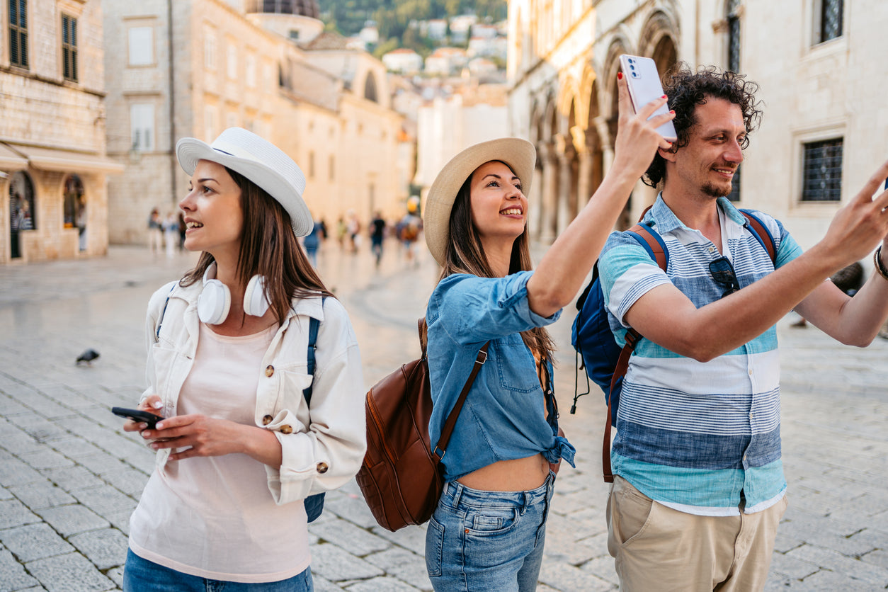 Zwei Frauen und ein Mann, die interessiert den städtischen Platz betrachten, auf dem sie gerade stehen und Fotos machen.