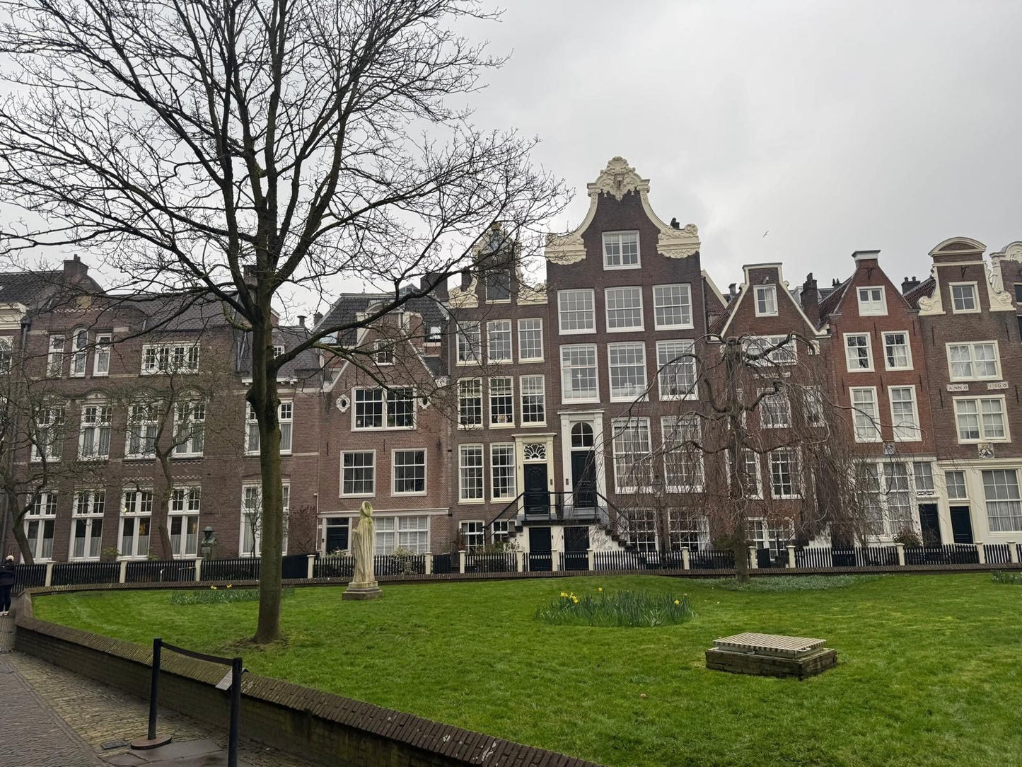 Der begrünte Innenhof des Begijnhof in Amsterdam mit historischen Wohnhäusern rund um eine Rasenfläche.