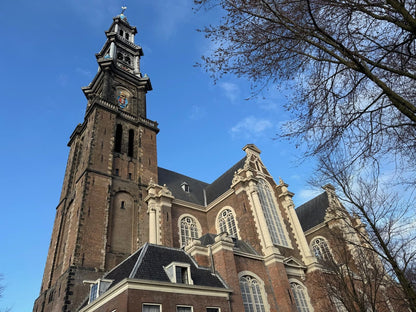 Die Westerkerk in Amsterdam mit dem Westertoren, dem höchsten Kirchturm der Stadt, vor blauem Himmel.