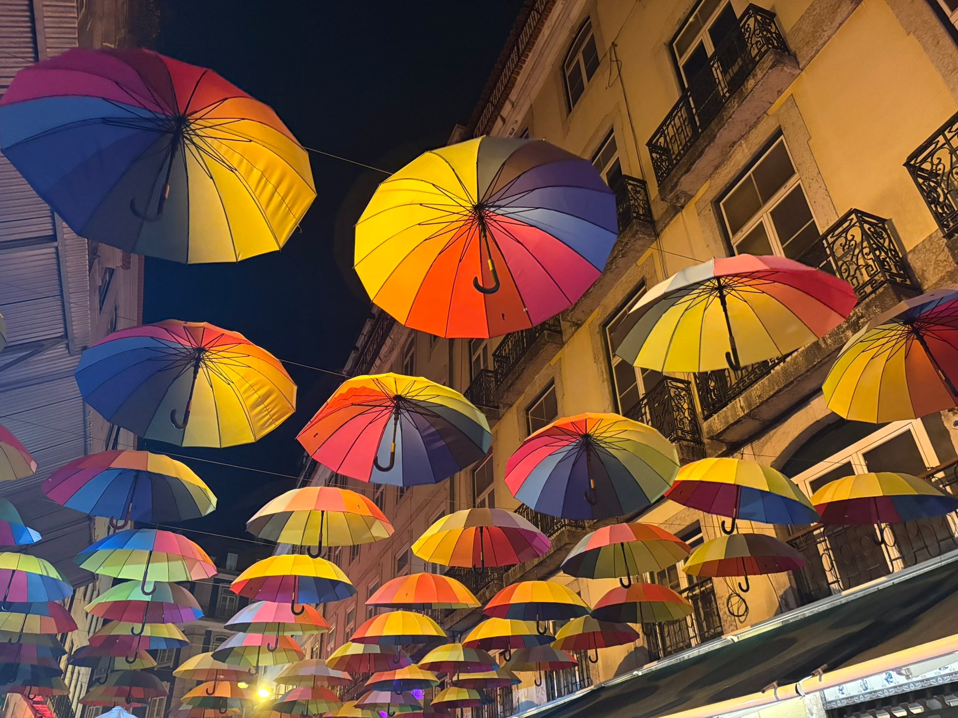 Ombrelloni colorati sospesi sopra un vicolo di Lisbona illuminato di sera
