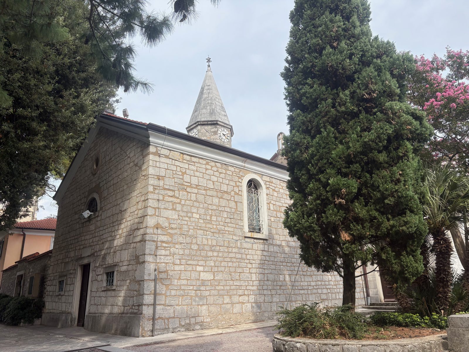 Die Abteikirche Crkva sv. Jakova in Opatija aus hellem Stein, daneben hohe Zypressen und blühender Oleander.