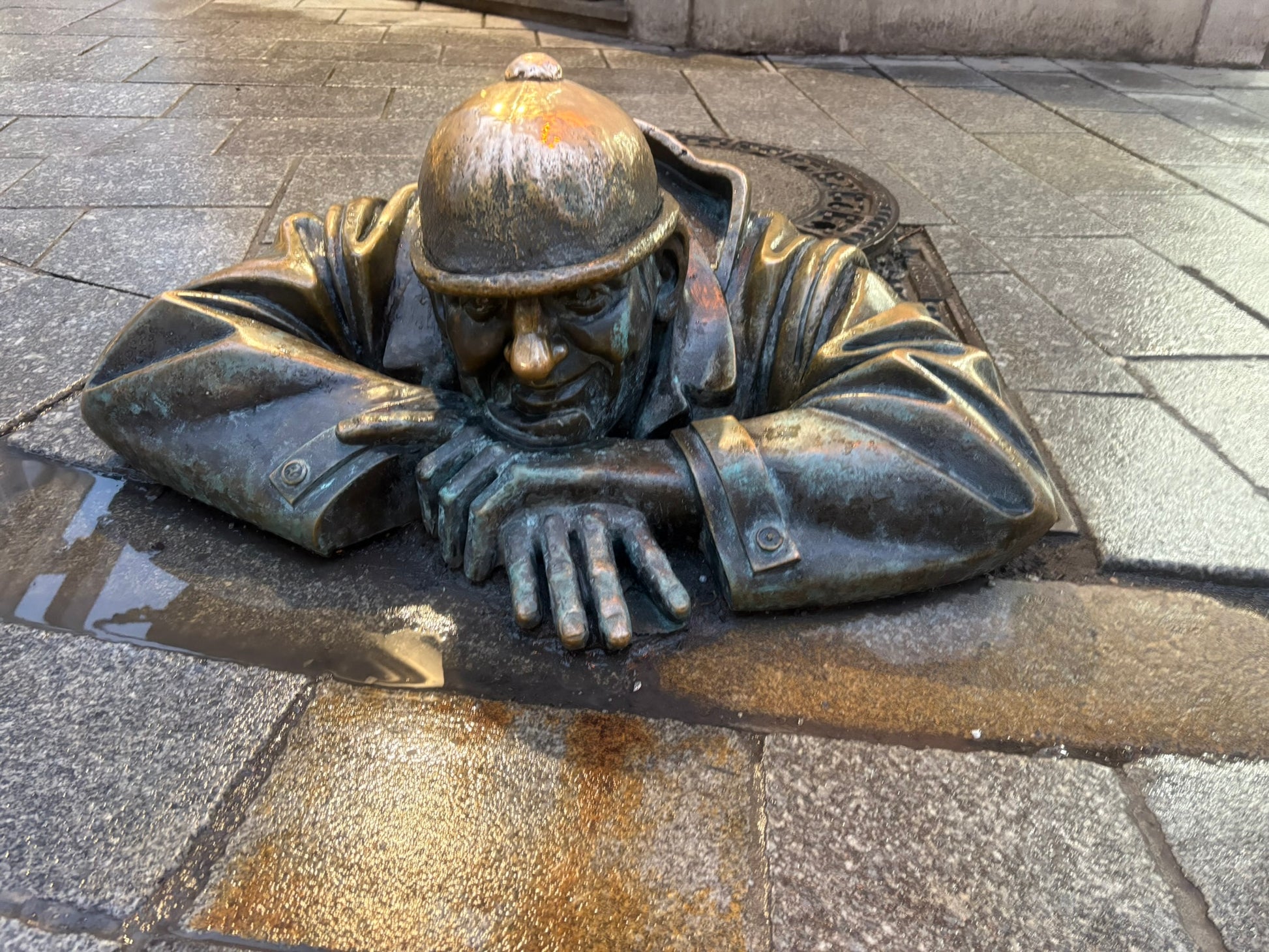 Statua di bronzo Čumil che spunta da un tombino nel centro storico di Bratislava