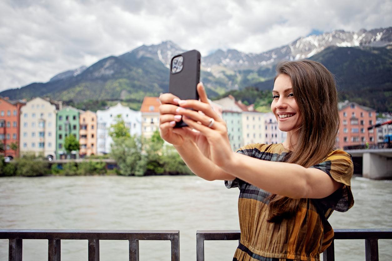 Woman taking a selfie in front of the colourful Mariahilf houses on the Inn in Innsbruck