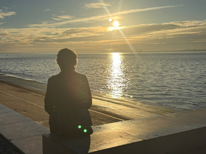 Una persona seduta sulla riva del Tago a Lisbona guarda il tramonto